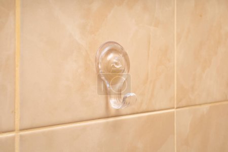 A clear suction hook attached to a beige tiled wall.