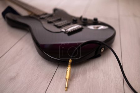 Foto de Una guitarra eléctrica negra conectada a un cable de audio en un suelo de madera. - Imagen libre de derechos