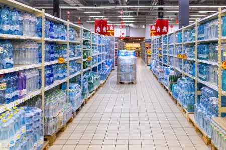 Photo for Kyiv, Ukraine - 03.07.2024: Shelves lined with various brands of bottled water in a Auchan supermarket with promotional signs, depicting consumer choice and plastic use. - Royalty Free Image
