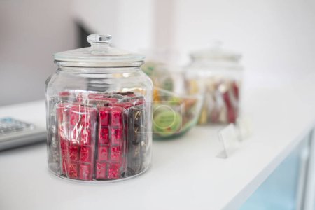 A transparent glass jar filled with a variety of colorful wrapped candies, neatly displayed on a white countertop in a bright, contemporary setting.