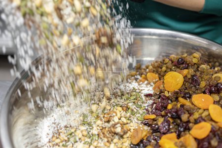 Téléchargez les photos : Personne versant de l'avoine dans un bol de fruits secs et de noix, préparant du muesli. - en image libre de droit