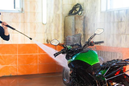 Teilansicht eines grünen Motorrads, das mit einem Hochdruckreiniger gereinigt wird, mit Fokus auf Wasserspray und Details.