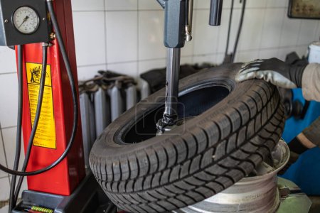 A tire technician debeading a tire from the wheel rim using specialized machinery at an automotive repair shop.