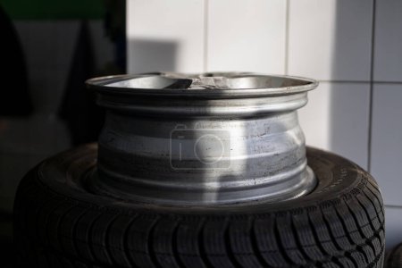 Eine Nahaufnahme einer silbernen Felge mit Schäden, die auf einem schwarzen Reifen in einer Werkstatt ruht.