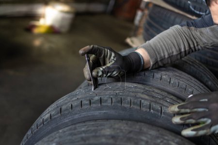 A mechanic's gloved hands using calipers to measure or assess the wear on a car tire in an automotive workshop.
