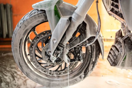 Close-up of a motorcycle's front wheel being washed with soapy foam, showcasing the cleaning process in detail.