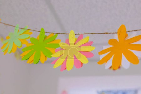Handmade colorful paper flowers hanging on a string, perfect for party decorations, DIY crafts, and festive events, adding a cheerful touch to any setting.