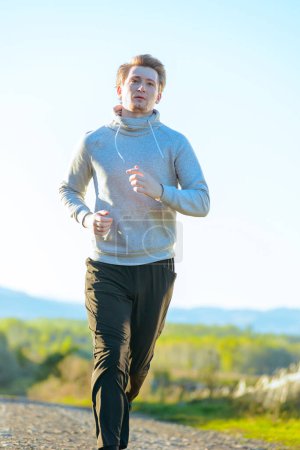 Téléchargez les photos : Courir homme jogging dans la nature rurale à la belle journée d'été. Sport fitness modèle caucasien ethnicité entraînement de plein air. - en image libre de droit