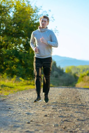 Foto de Hombre corriendo corriendo corriendo en la naturaleza rural en un hermoso día de verano. Deporte fitness modelo caucásico etnia entrenamiento al aire libre. - Imagen libre de derechos