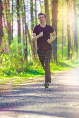 Photo for A man wearing a hat is jogging along an asphalt road surrounded by grass and trees in the woods for leisure and recreation - Royalty Free Image