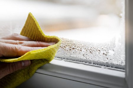 Photo for High humidity in the house. hand wipes off water condensation from plastic window glass in the room. home moisture - Royalty Free Image