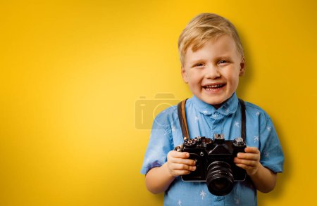 Foto de Pequeño niño sonriente con cámara retro sobre un fondo amarillo con espacio para copiar. fotógrafo infantil - Imagen libre de derechos