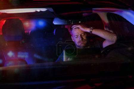 Téléchargez les photos : Homme désespéré assis à l'intérieur d'une voiture après avoir été arrêté par la police pour violations de la circulation sur la route la nuit - en image libre de droit