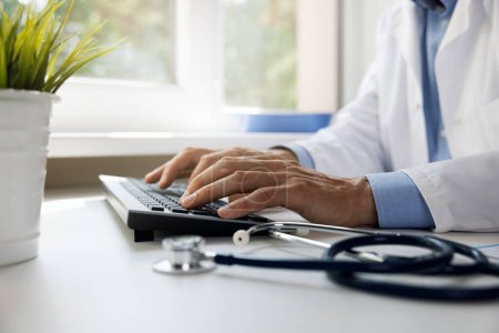 Foto de Doctor escribiendo en el teclado de la computadora. trabajando en la clínica. consulta médica en línea y concepto de salud electrónica - Imagen libre de derechos