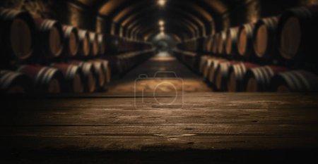 Foto de Mesa vacía de madera oscura para la exhibición del producto sobre fondo de bodega borrosa de barricas de vino - Imagen libre de derechos