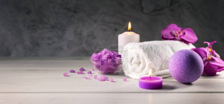Foto de Bomba de baño púrpura, cristales de sal marina, toalla y velas perfumadas en la mesa de madera. centro de spa de bienestar. banner con espacio de copia - Imagen libre de derechos