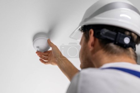 Foto de Trabajador instalando detector de humo fotoeléctrico en el techo de la casa. seguridad en el hogar y sistema de alarma contra incendios - Imagen libre de derechos