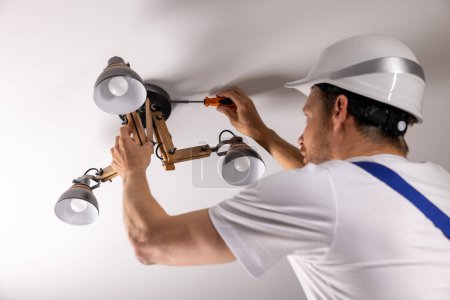 Foto de Servicios de manitas. electricista instalando lámpara de techo en casa - Imagen libre de derechos