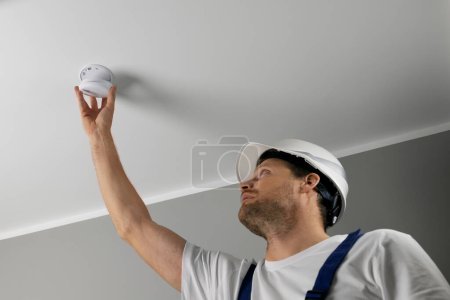 Foto de Ingeniero de seguridad contra incendios instalando detector de humo fotoeléctrico en el techo de la casa. seguridad en el hogar y sistema de alarma contra incendios - Imagen libre de derechos