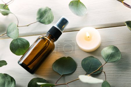 Foto de Frasco de perfume en blanco con hojas de eucalipto y vela sobre mesa de madera blanca - Imagen libre de derechos