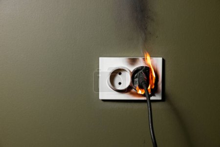 Foto de Enchufe eléctrico de pared ardiente con cable de electrodoméstico enchufado de cortocircuito en la casa. concepto de seguridad contra incendios y sobrecarga de energía en el hogar - Imagen libre de derechos