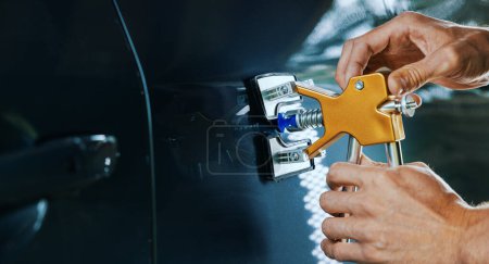 Reparatur von Lackschäden am Auto. Mann fixiert Fahrzeugtüre mit PDR-Technologie-Werkzeug