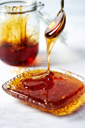 Dicker goldener Sirup oder Karamell oder Honig tropfen vom Löffel in den Teller. Weißer Hintergrund. Hochwertiges Foto