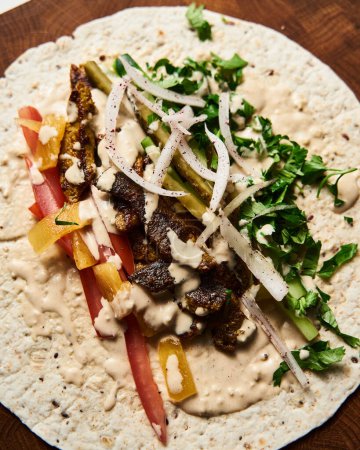 Photo for Beef and Lamb Lebanese style shawarma with onions, greens and vegetables such cucumber and tomato. all seasoned with tahini and garlic sauce and wrapped in pita or pita bread. High quality photo - Royalty Free Image