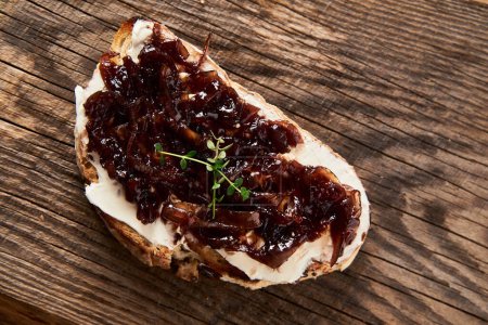 Delicious French Appetizer Freshly Cooked Onion Confit on toast with cream cheese and thyme. Wood board and jar with onion marmalade. Concrete loft background. . High quality photo