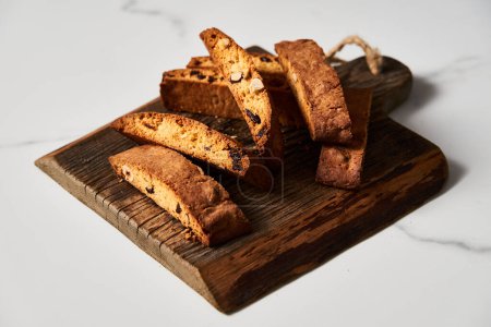 Assortiment de biscotti aux amandes et aux canneberges sur une planche en bois rustique, agrémentée d'un décor en marbre. Photo de haute qualité