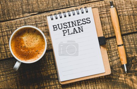 Téléchargez les photos : Plan d'affaires Word dans un carnet de bureau sur une table en bois à côté d'une tasse à café. - en image libre de droit