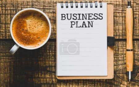 Téléchargez les photos : Plan d'affaires Word dans un carnet de bureau sur une table en bois à côté d'une tasse à café. - en image libre de droit