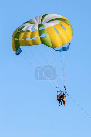 Téléchargez les photos : FIUMEFREDDO DI SICILIA, SICILY, ITALIE - 12 AOÛT 2022 Un couple noir en maillot de bain et gilet de sauvetage tiré et volant avec un parachute jaune près du rivage - en image libre de droit