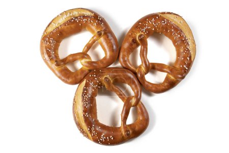 Foto de Tres pretzel bávaro vista superior con sal sobre un fondo blanco. El pretzel tiene la forma de un nudo, y está cubierto de una generosa cantidad de sal. El pretzel es de color marrón dorado, y se ve crujiente y delicioso. - Imagen libre de derechos