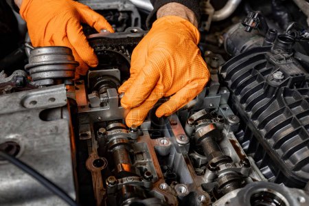 Photo for Detailed view of a car mechanic's hands, protected by orange gloves, as they attentively work on repairing an opened car engine in an auto service - Royalty Free Image