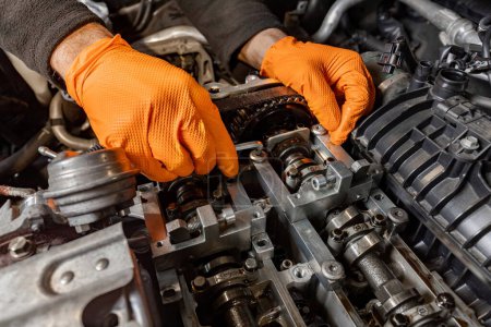 Photo for Experience the precision of a skilled mechanic's hands, clad in orange gloves, as they meticulously work under the hood to repair an open car engine in an auto service center, ensuring top-notch maintenance - Royalty Free Image