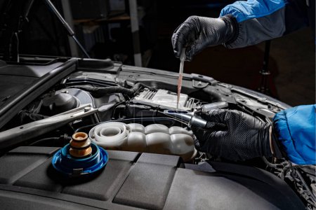 Witness the precision of a mechanic's gloved hands as they carefully extract brake fluid from under the hood using a disposable pipette, placing it onto the refractometer lens to verify the brake fluid concentration