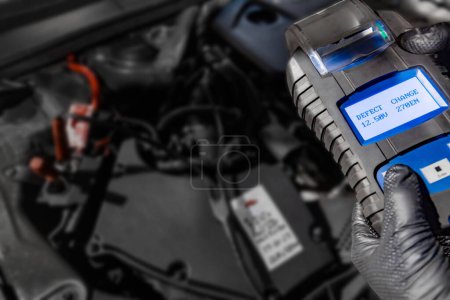 Photo for Explore automotive diagnostics as a mechanic holds a battery tester under the hood, displaying Defect and Change on the screen above the car battery, indicating the need for replacement. Ensure optimal vehicle performance with timely battery maintena - Royalty Free Image