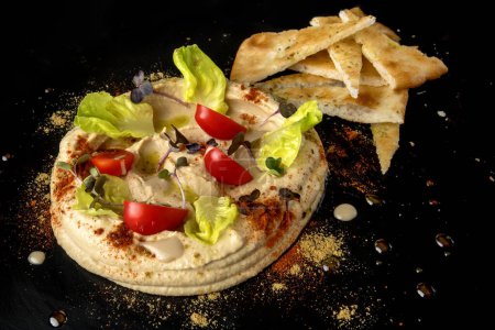 Photo for Indulge in a captivating hummus presentation, with smooth hummus forming a circular centerpiece adorned with juicy tomato slices, fresh green salad, and vibrant microgreens, all delicately dusted with paprika. Complemented by crispy pita bread slices - Royalty Free Image
