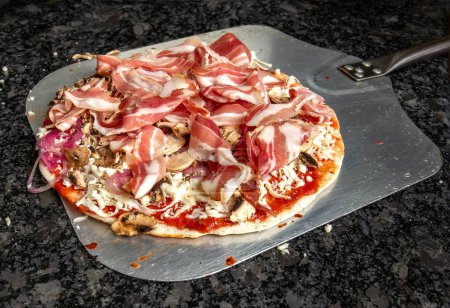Photo for Irresistible pizza topped with ham, mushrooms, cheese, onions, and ketchup, poised on a stainless steel peel on a granite table, ready for the oven. Get ready for a burst of flavors in every bite - Royalty Free Image