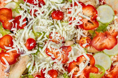 Photo for An up-close shot of a vegetarian pizza before baking, featuring mozzarella cheese, tomatoes, red and green bell peppers, and slices of cucumber, arranged beautifullyon the dough - Royalty Free Image