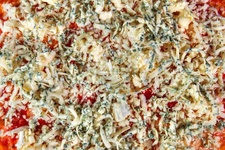Photo for A tantalizing close-up view of a pizza prepared for the oven, showcasing its delicious toppings of tomato sauce, grated cheese, and finely chopped basil. With no visible crust, this pizza promises a mouthwatering experience. - Royalty Free Image