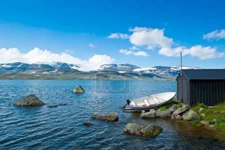 Beautiful landscape with a boat on the shore of Lake Finsevatnet, snowy mountains and glacier Hardangerjokulen in Finse, Norway