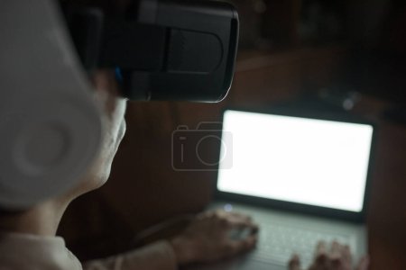 Téléchargez les photos : Jeune homme portant des lunettes de réalité virtuelle et des écouteurs à la maison profitant d'un cyberespace immersif - en image libre de droit
