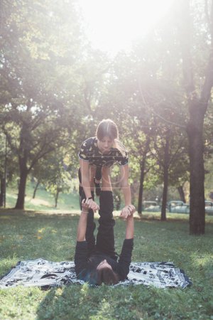 Foto de Dos deportistas sanos practicando yoga acrobático blancing estiramiento ejercicio en el jardín - Imagen libre de derechos