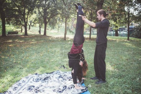 Téléchargez les photos : Instructeur professionnel de yoga masculin aide les débutantes à faire acrobatique position outtoors parc - en image libre de droit