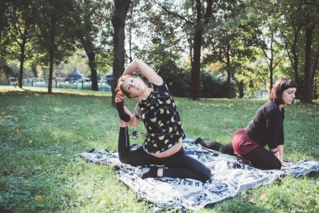 Foto de Mujeres deportivas flexibles al aire libre estirando y practicando yoga al aire libre jardín parque - Imagen libre de derechos