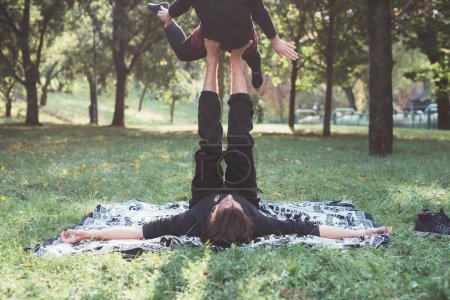 Photo for Healthy young man lying on grass and balancing woman doing acrobatic yoga exercise in park - Royalty Free Image