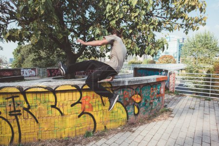 Photo for Acrobatic athletic sportive young man outdoors jumping above obstacle running training parkour - Royalty Free Image