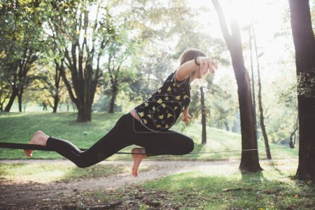 Téléchargez les photos : Stunt femme en forme athlétique à l'extérieur pratiquant relâchement équilibrage sur corde raide - en image libre de droit
